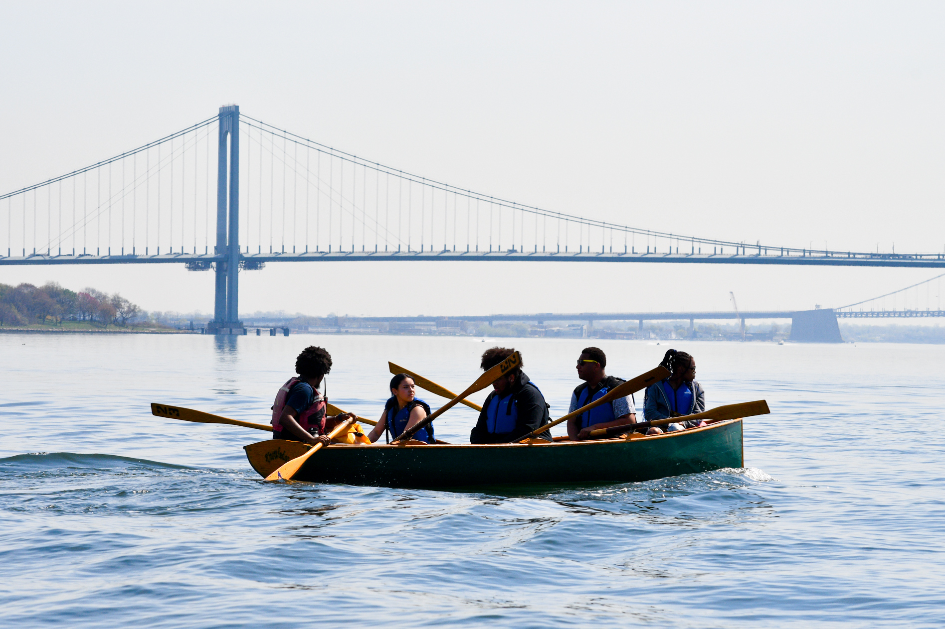 a group of kids row on the bronx river in front of a bridge